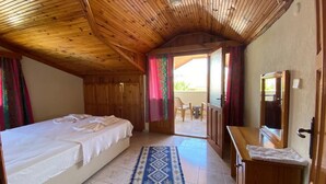 A bedroom with a bed, wooden ceiling, a small desk, and a view to an outdoor area.