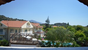 A coastal hotel with a pool, a covered outdoor area, and a mountain in the background.