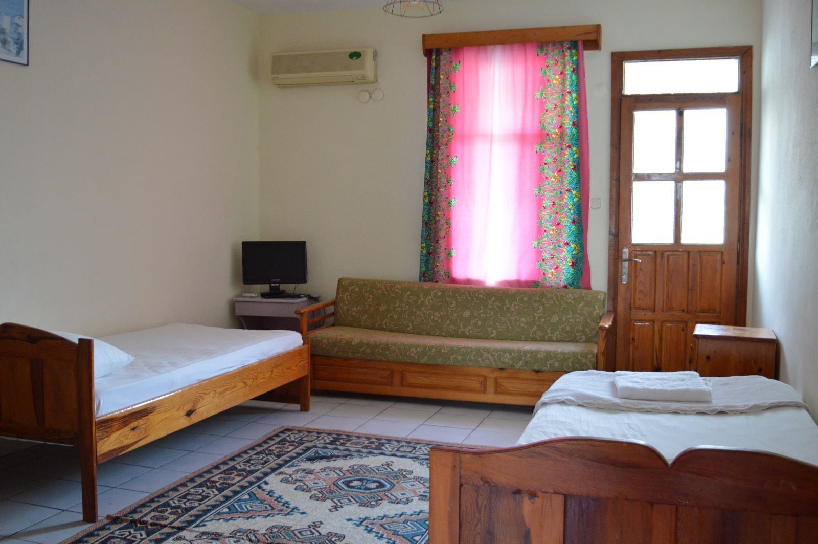 A room with two wooden beds, a sofa, a television, and a window with curtains.