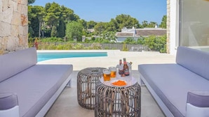 A poolside area with two wicker tables, a sofa, and a view of a swimming pool and greenery. - Casa Bio Nueva: Super sea views, heated pool, 100MB wifi, A / C (Jávea)