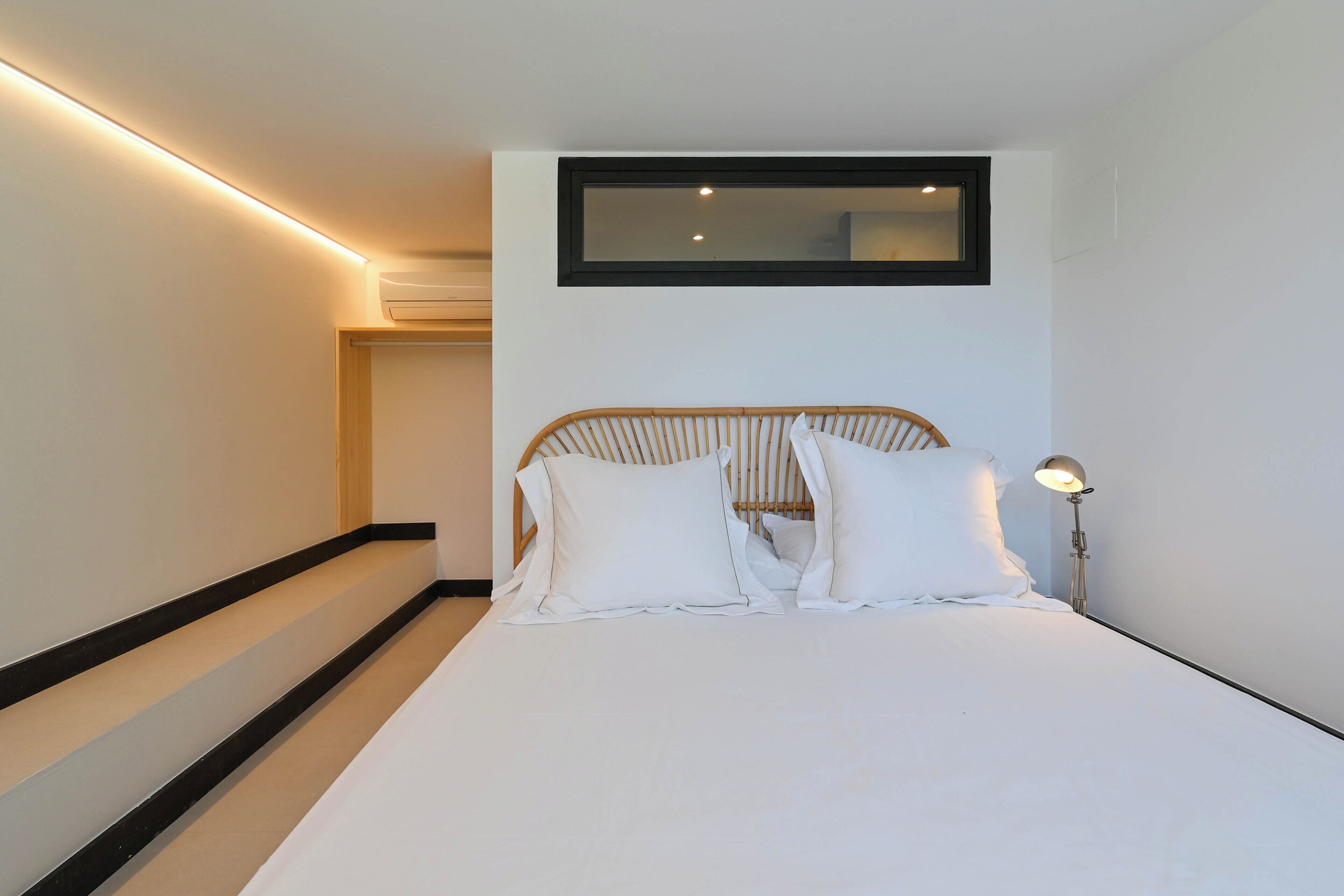 Un dormitorio con cama, mesita de noche, lámpara y ventana.