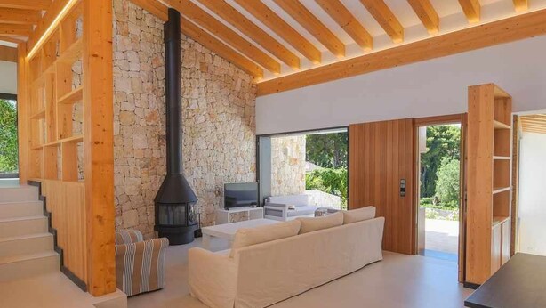 A modern interior with a stone wall, wooden beams, a fireplace, a sofa, and a TV. - Casa Bio Nueva: Super sea views, heated pool, 100MB wifi, A / C (Jávea)