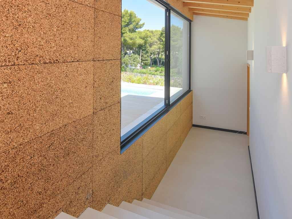 Un interior moderno con una escalera que lleva a un balcón, un ventanal grande y vistas de la vegetación al exterior.