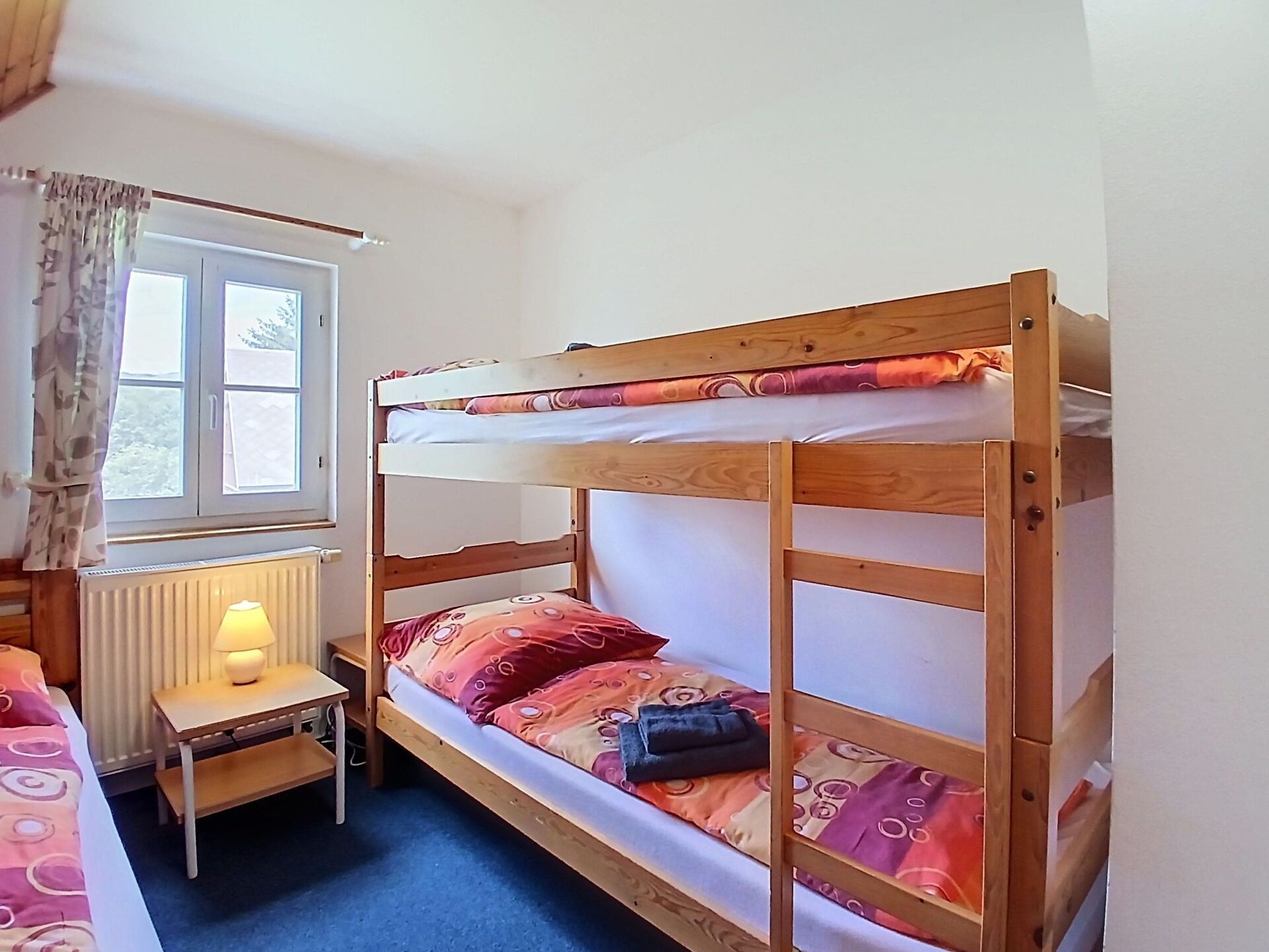 Un lit superposé avec un bureau et une lampe, une fenêtre avec des rideaux et un radiateur.