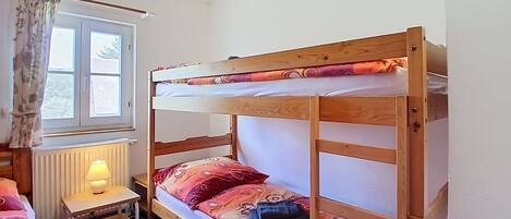 Un lit superposé avec un bureau et une lampe, une fenêtre avec des rideaux et un radiateur.