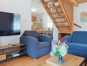 A living room with a sofa, a coffee table with a vase of flowers, a television, and a staircase.