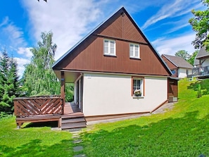 A two-story house with a sloped roof, a porch with a wooden railing, and a small garden area.