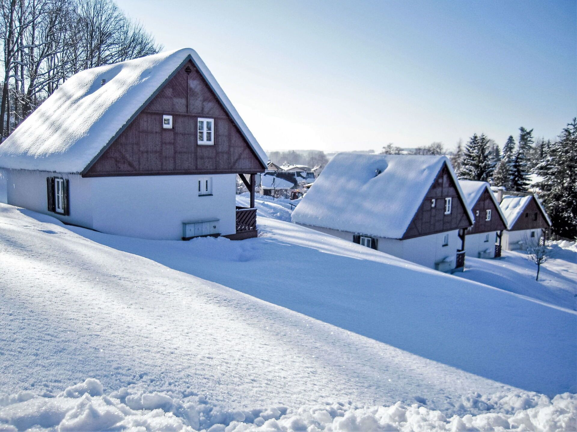 Un village enneigé, avec ses maisons traditionnelles en bois, un ciel dégagé et un paysage vallonné.