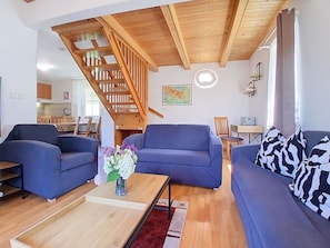 A modern living room with a wooden staircase, two sofas, a coffee table with a vase of flowers, and a dining area in the background.