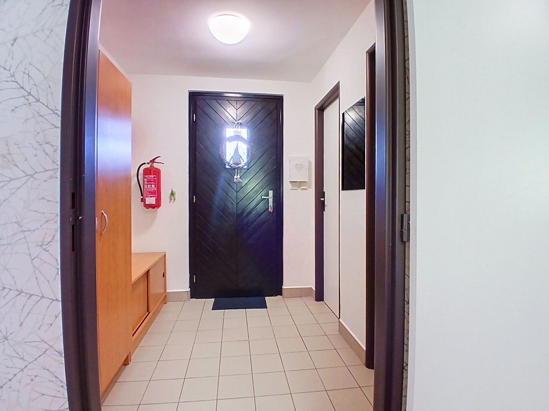 A hallway with a black door, a fire extinguisher, and a bench.