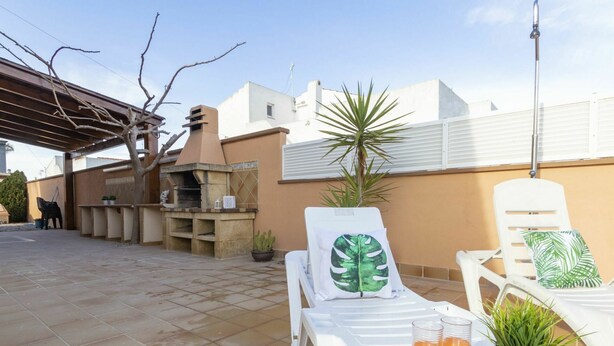 Une terrasse équipée d’un barbecue, de chaises longues et d’une table où sont disposées des boissons et des plantes.