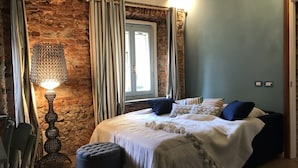 A bedroom with a stone wall, a bed with white bedding and blue pillows, a hanging lamp, and a window with curtains.