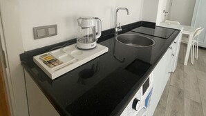 A compact kitchen with a black countertop, a coffee maker, a sink, and a white cabinet above. - Muharrem Bey Butik Otel (Cesme)