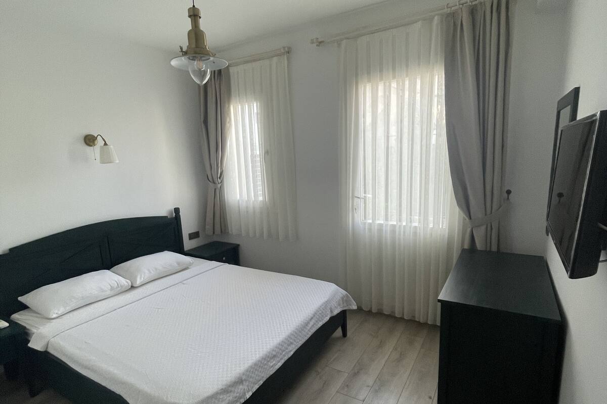 A bedroom with a bed, a nightstand, a dresser, a ceiling fan, and a window with curtains.