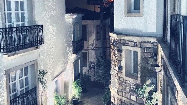 A narrow alleyway with buildings on either side, featuring balconies with black railings and a staircase leading down. - Muharrem Bey Butik Otel (Cesme)