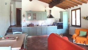 A cozy living room with a wooden ceiling, a dining area with a table and chairs, and a kitchen with light blue cabinets and a stove. - Villa for groups and families, with Private Pool in Monteverdi Marittimo (Monteverdi Marittimo)