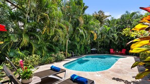 Uma área de piscina com hidromassagem, espreguiçadeiras e churrasqueira.