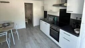 A modern kitchen with white cabinets, a black stove, and a dining area with a table and chairs. - Maxima Sunset WAIKIKI 4 pers (Sainte-Maxime)