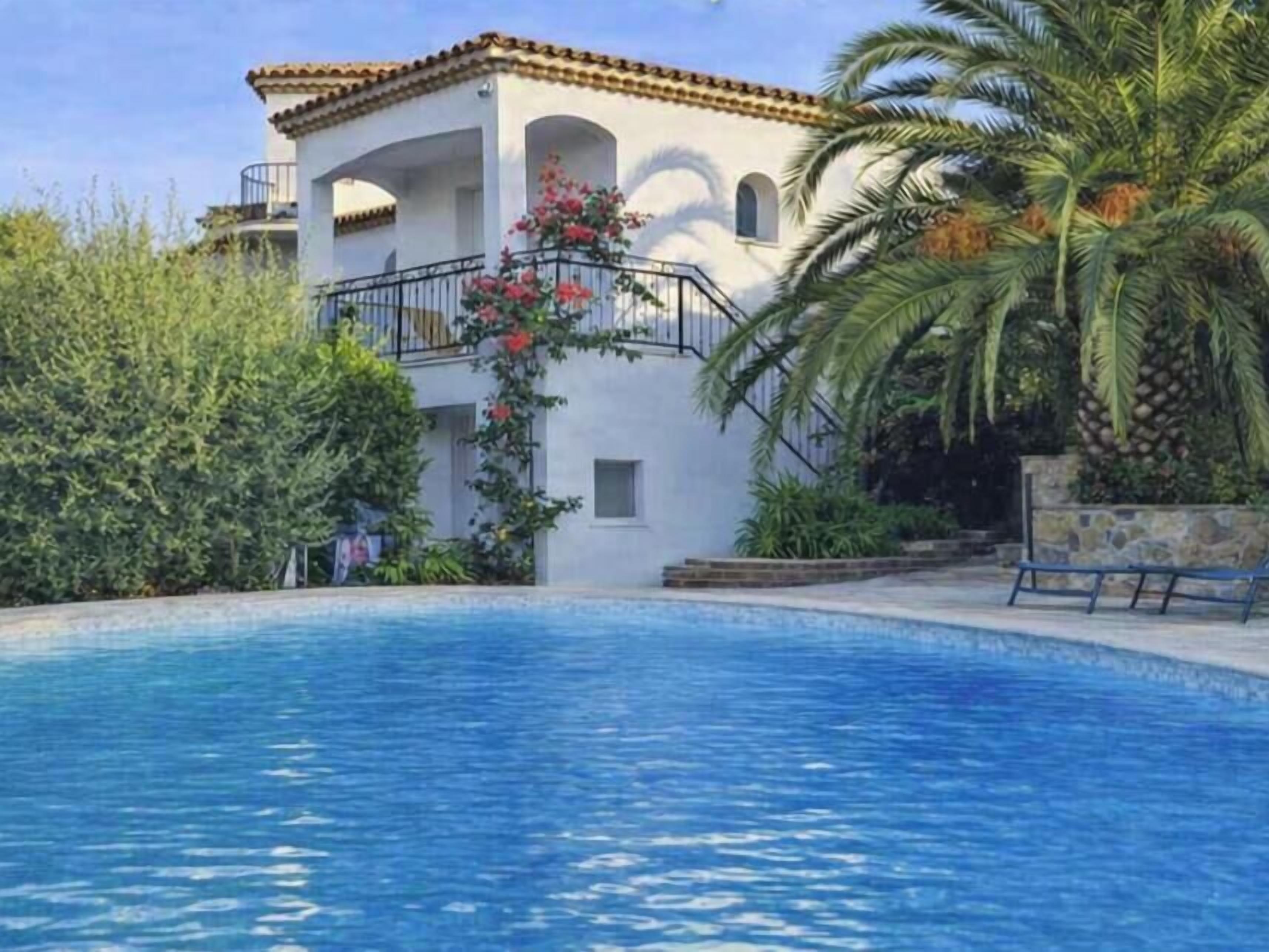 A pool with a white building in the background, surrounded by greenery.