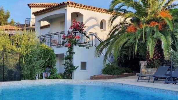A swimming pool area with a white building, palm trees, and a balcony with pink flowers. - Maxima Sunset WAIKIKI 4 pers (Sainte-Maxime)