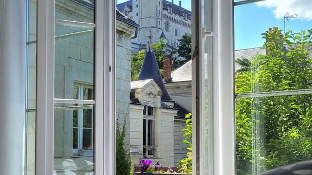 A bedroom with a large window overlooking a historic building with a tower. - Splendid view of the Château and the Loire (Saumur)