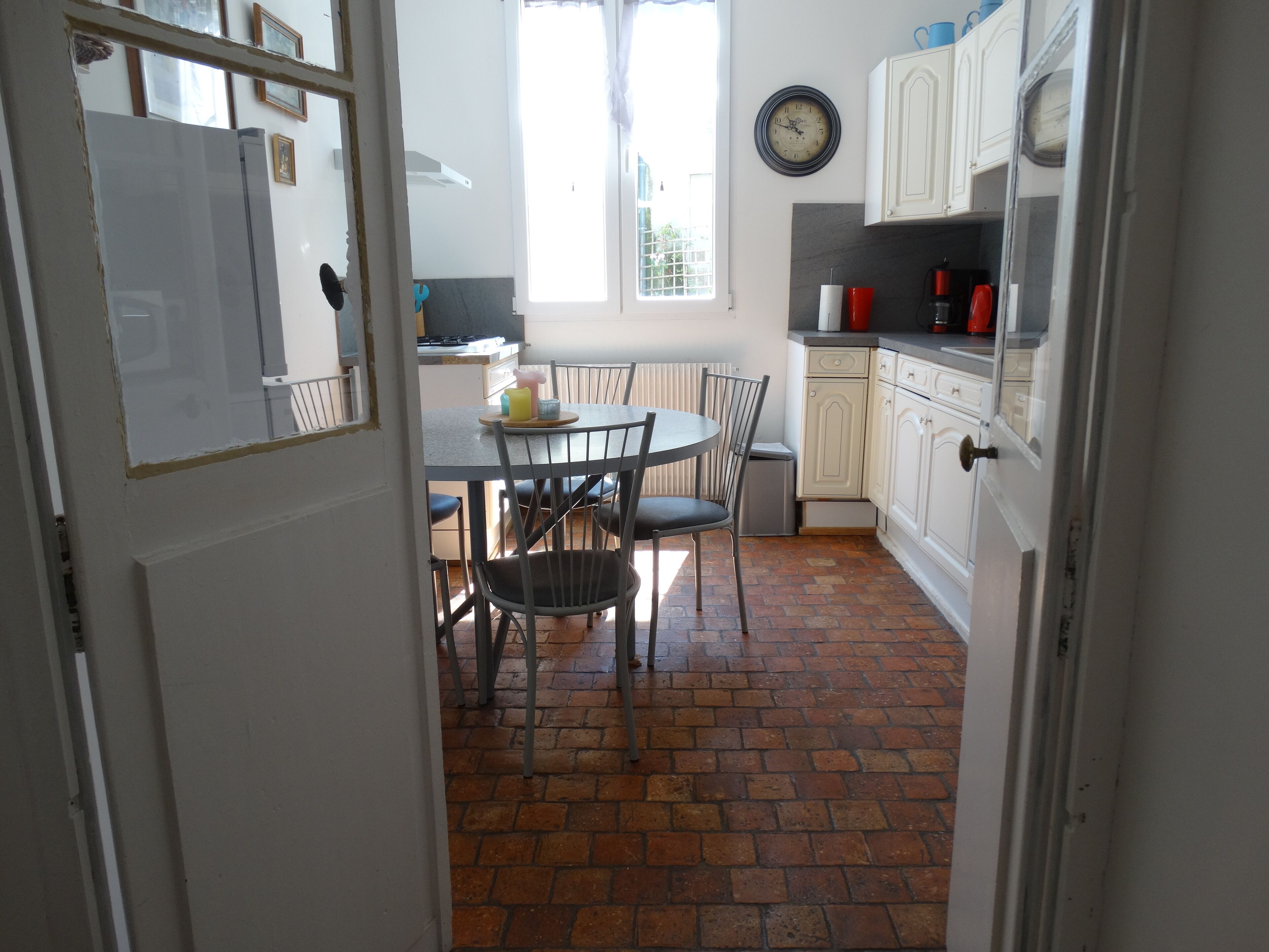 A kitchen with a dining table, chairs, a clock, and cabinets.
