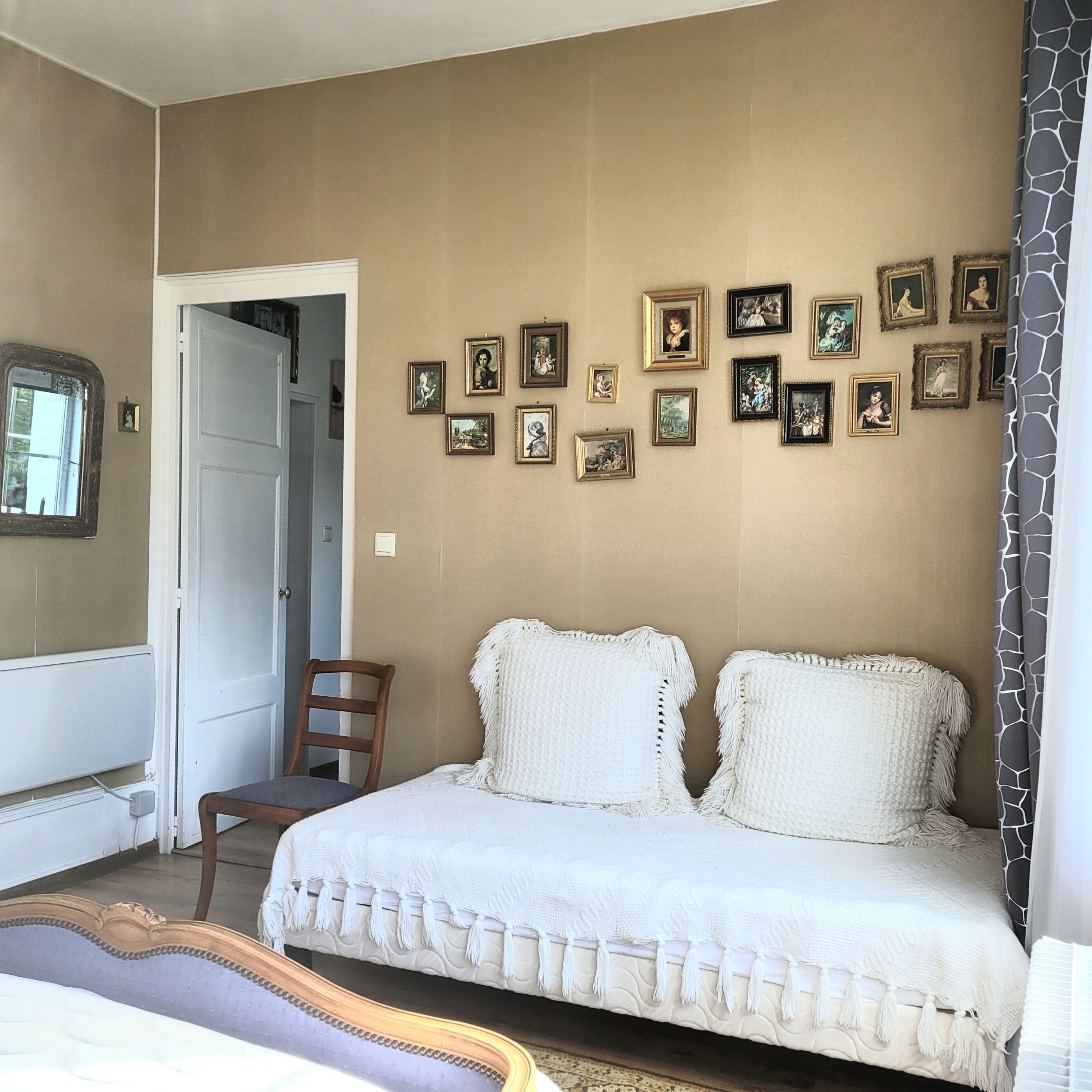 A bedroom with a bed, a chair, and a wall adorned with framed pictures.