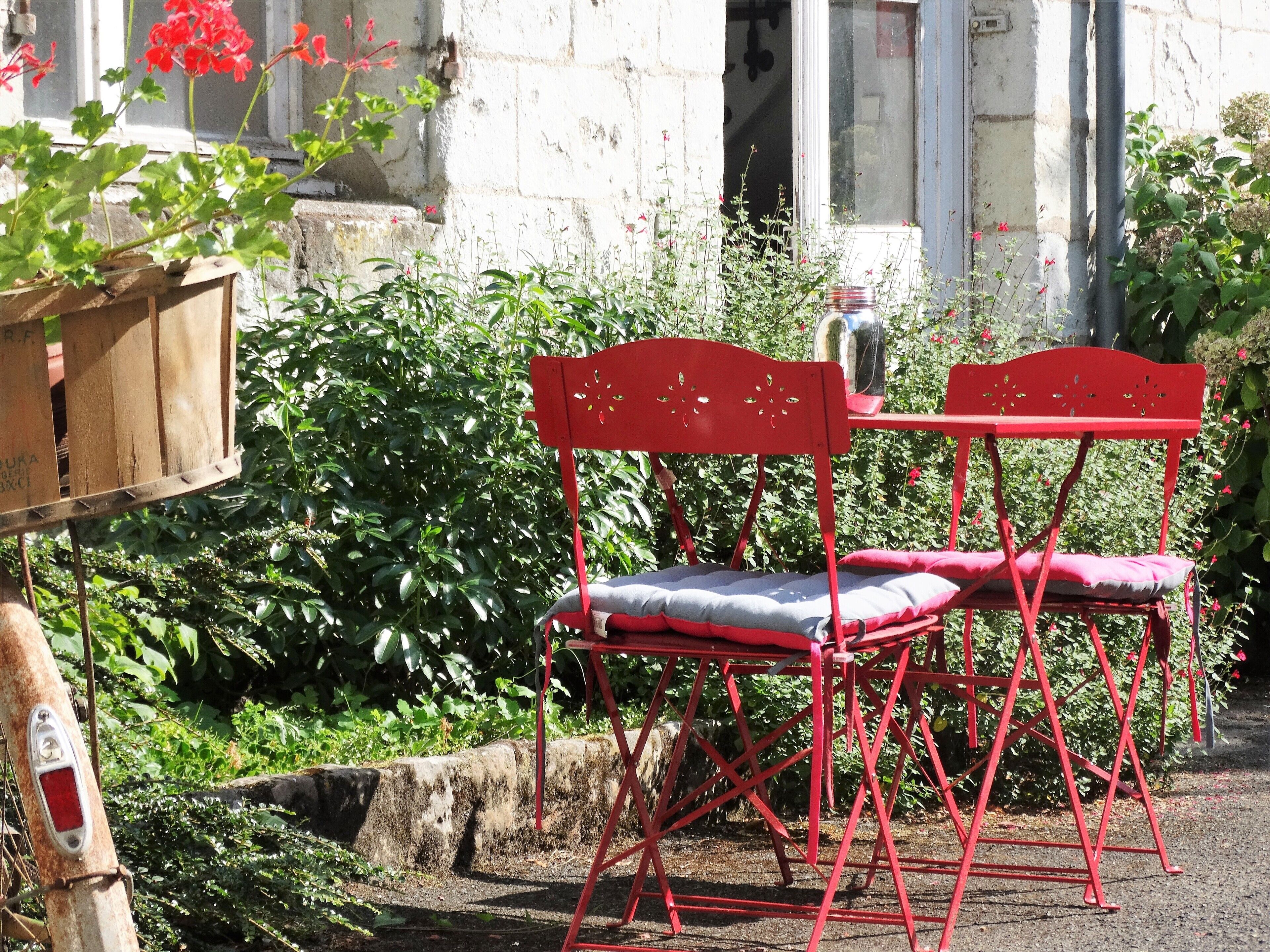 A red metal chair with a cushion, placed outdoors with a stone wall and greenery in the background.