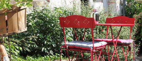 A red metal chair with a cushion, placed outdoors with a stone wall and greenery in the background.