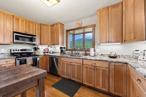 Una cocina con armarios de madera, microondas, estufa, lavavajillas y una ventana con vistas al exterior.