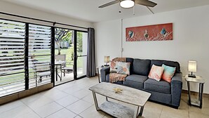 Een moderne woonkamer met een grijze bank, een houten salontafel en een groot raam met zonwering.