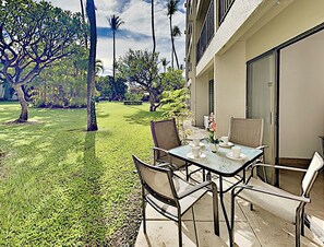 A patio with a table and chairs, surrounded by a well-maintained lawn and palm trees. - Where Maui Shines Renovated Kihei Condo Across From Kamaole Beach Pool (Kihei)