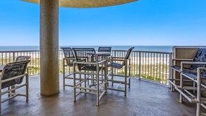 A covered outdoor seating area with chairs and tables, overlooking a beach.
