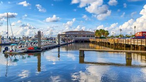 A marina with boats docked, a covered building, and a wooden walkway over water.