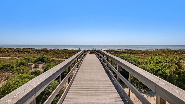 A wooden boardwalk leading to a beach with clear skies.