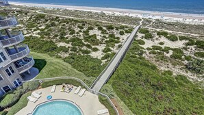 A beachfront property with a swimming pool, a bridge connecting to the beach, and a multi-story building with balconies.