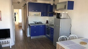 A compact kitchen with blue cabinets, a microwave, and a refrigerator. There's a dining table with chairs and a TV in the corner. - T2 comfortable Marina de Canet Plage (Canet-en-Roussillon)