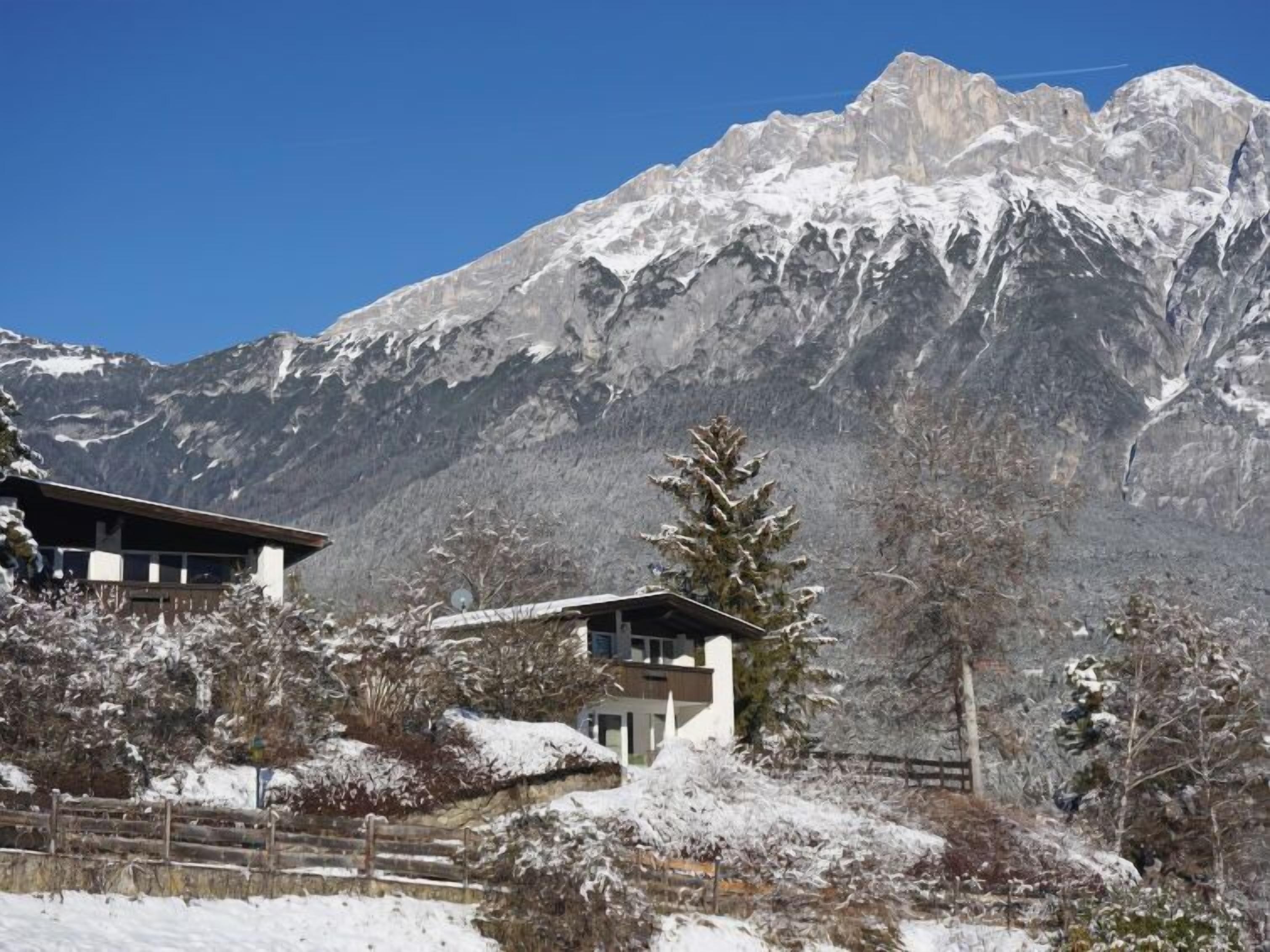 A mountain lodge with a modern design, featuring a large windowed room and a view of snow-covered peaks.
