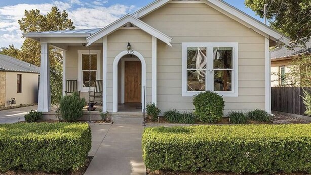 Une maison de plain-pied avec un porche à l’avant, un hall d’entrée abrité et un petit jardin devant, bordé de haies.