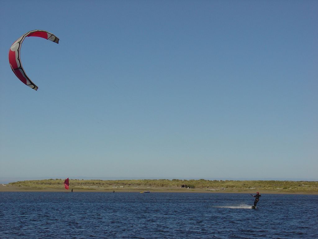 A person windsurfing on a body of water with a clear sky.
