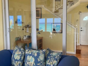 A room with a view of the ocean, a wooden table with items on it, and a blue sofa with patterned cushions. - Second Wind - Ocean Front - 2 Bedroom (Utila)