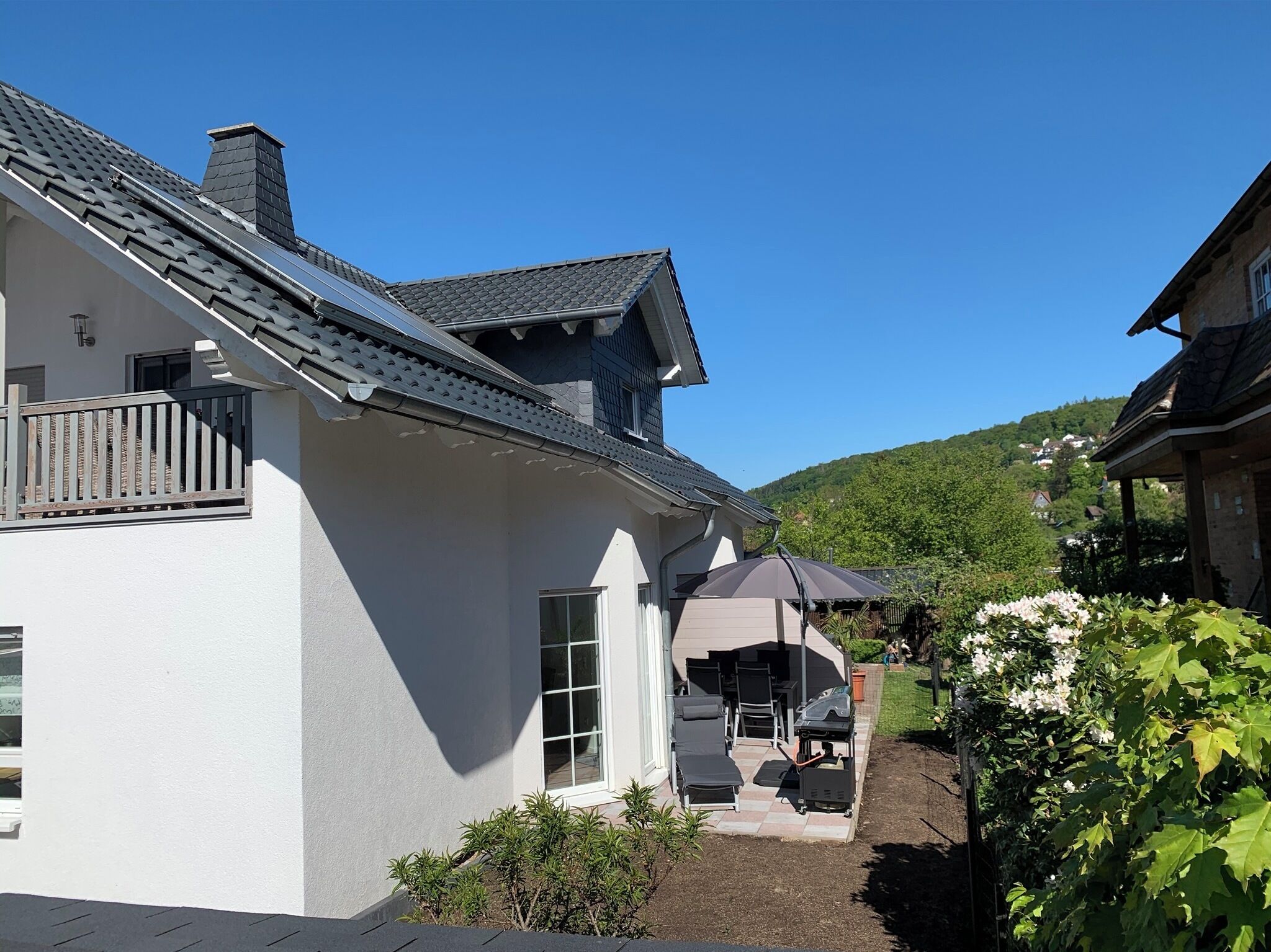Ein weißes Gebäude mit grauem Dach, einem Balkon und einer Terrasse mit Gartenmöbeln.