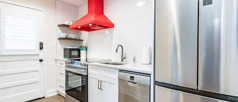 Una cocina moderna con electrodomésticos de acero inoxidable, armarios blancos y una campana extractora roja.