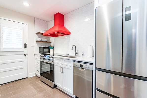 A modern kitchen with stainless steel appliances, white cabinetry, and a red hood.