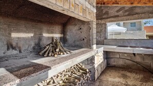 A stone fireplace with logs, a window overlooking a building, and a wooden ceiling.