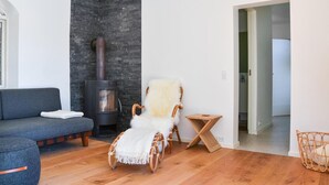 Ein modernes Wohnzimmer mit einer Steinwand, einem Kamin, einem grauen Sofa, einem weißen, flauschigen Sessel und einem Korbtisch.