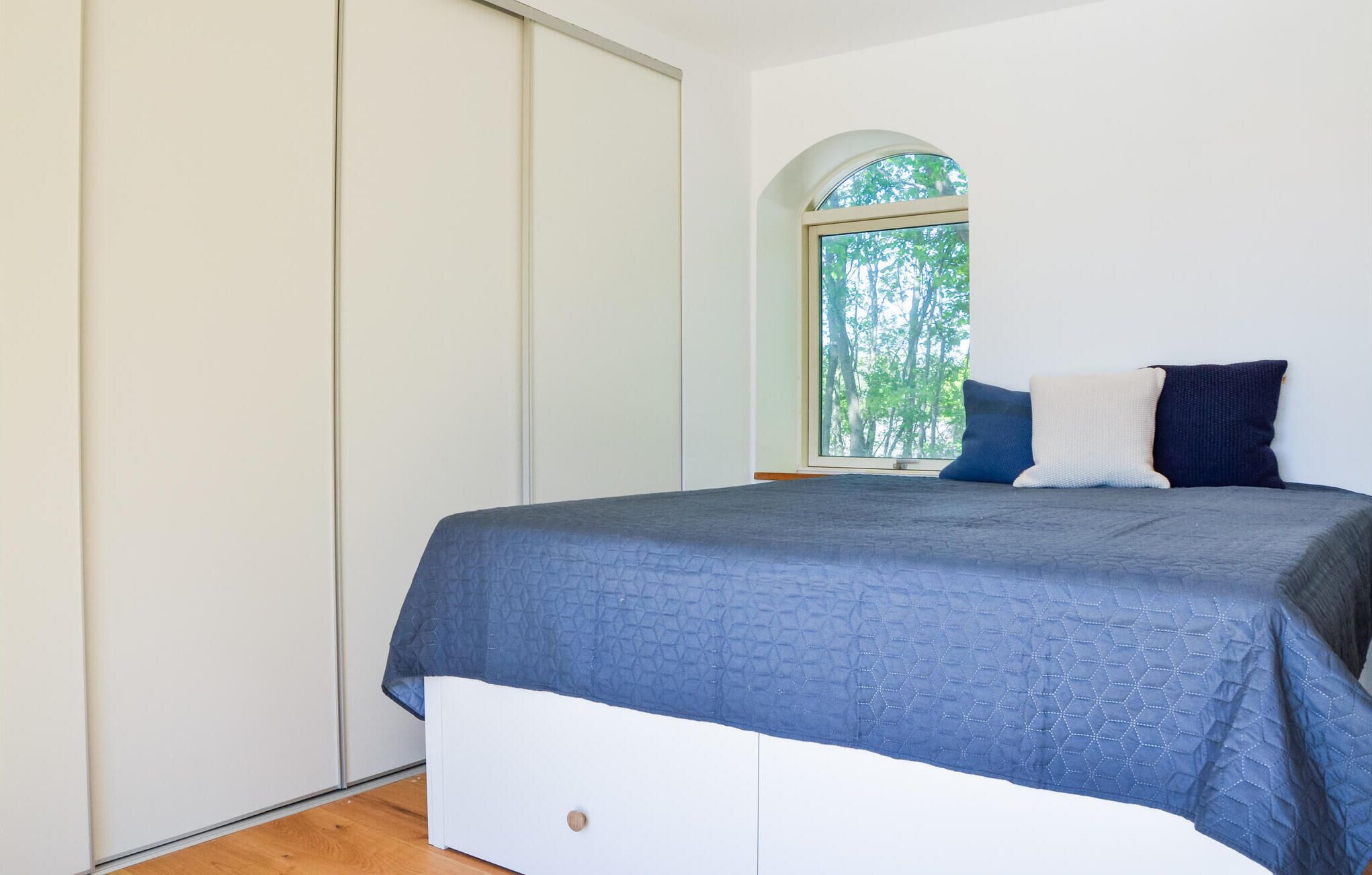 Une chambre à coucher avec un lit, une fenêtre donnant sur des arbres et une porte coulissante.