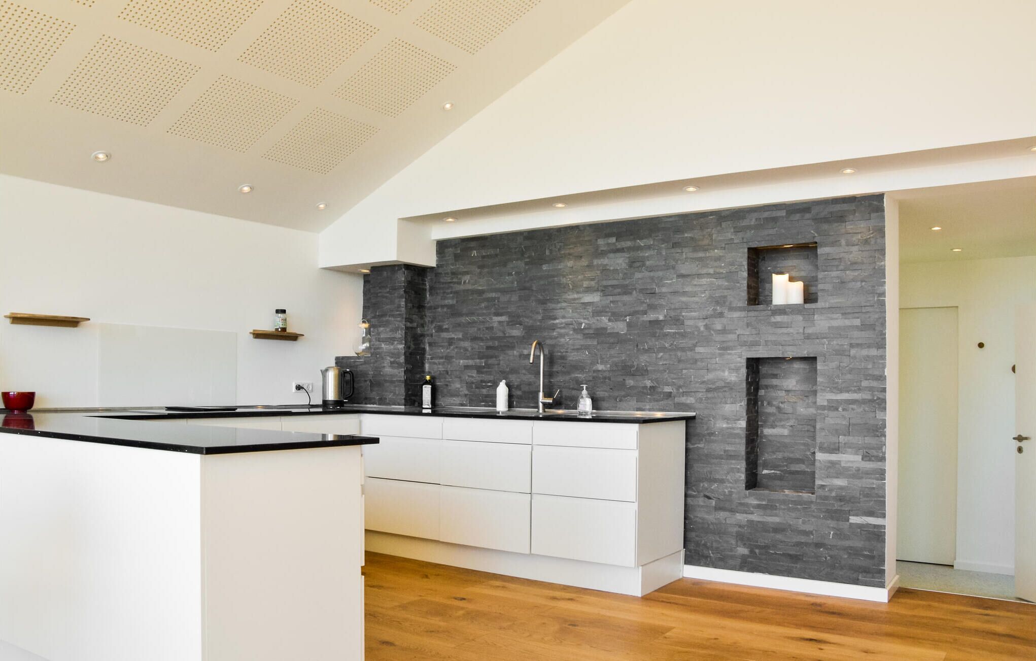 Eine moderne Küche mit schwarzem Steinrückwand, weißen Schränken und Holzboden.