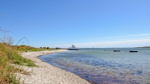 Ein sandiger Strand mit ruhigem Wasser, ein großes Boot und einige kleinere Boote in der Ferne.