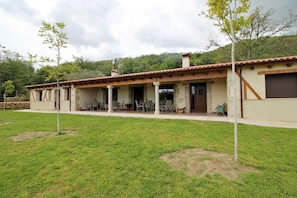 A two-story building with a tiled roof, a covered patio with outdoor seating, and a grassy lawn. - Hotel Rural San Giles (Aldeanueva de la Vera)